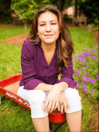 Woman sitting outdoors in a garden with purple flowers, smiling.
