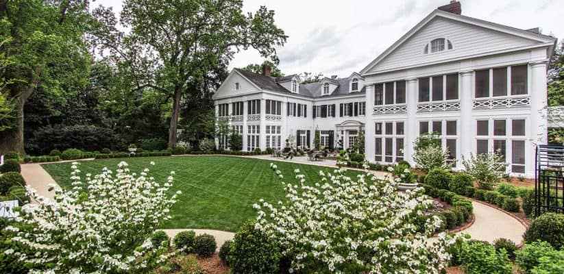 Beautiful white mansion surrounded by lush garden and blooming flowers in spring.