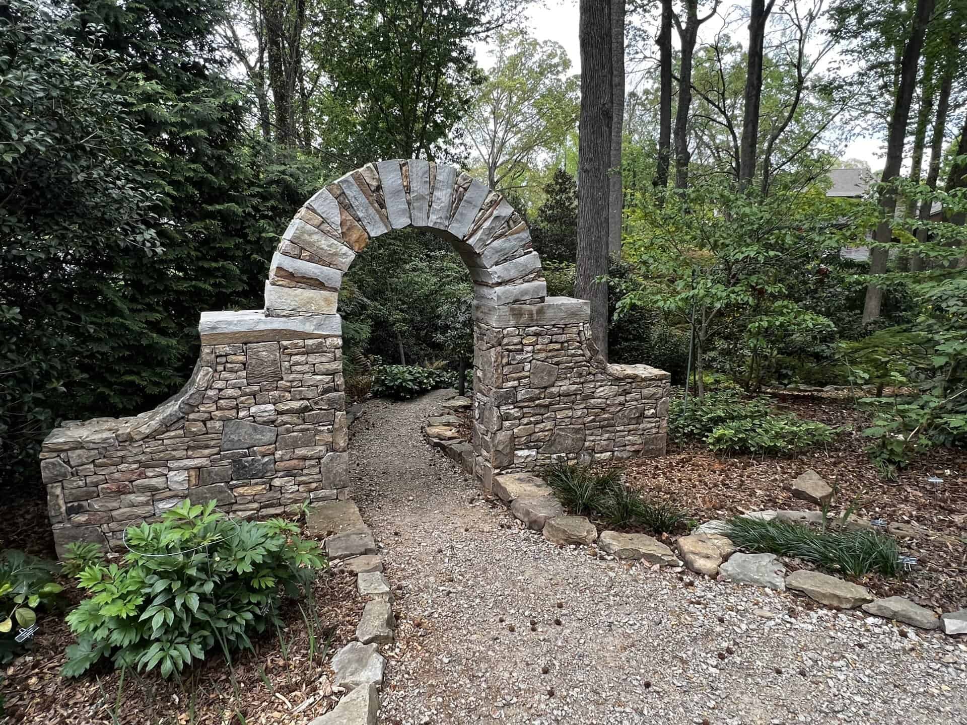 Charlotte Garden Club archway with stone construction in a lush garden setting.