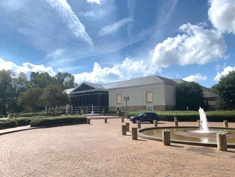 Charlotte Garden Club building with fountain and parking area under a blue sky.